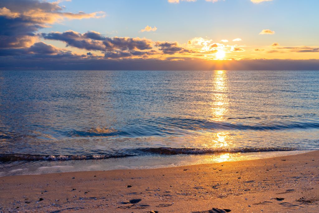 Beach at sunset with orange reflections on the waves and wet sand.