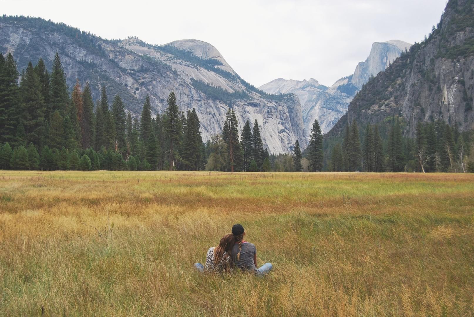Couple sitting in a grassy field overlooking a mountain valley.