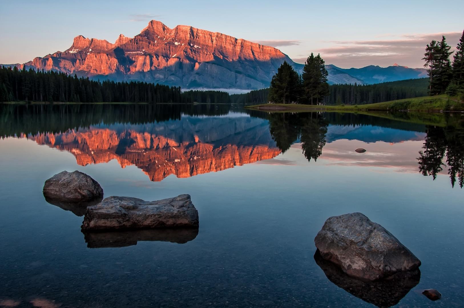 Mountain landscape with a lake reflecting an illuminated mountain range at twilight.