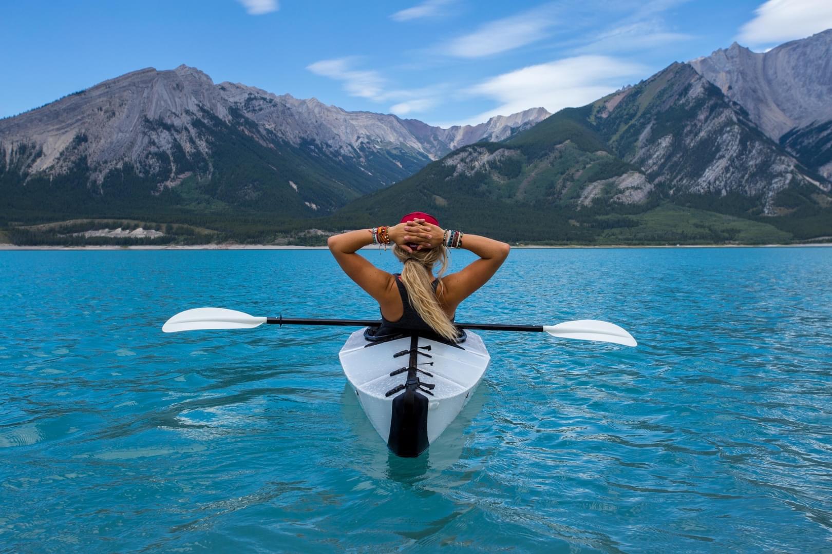 Reviewer profile picture: woman in a kayak relaxes on a turquoise lake with mountains in the background.