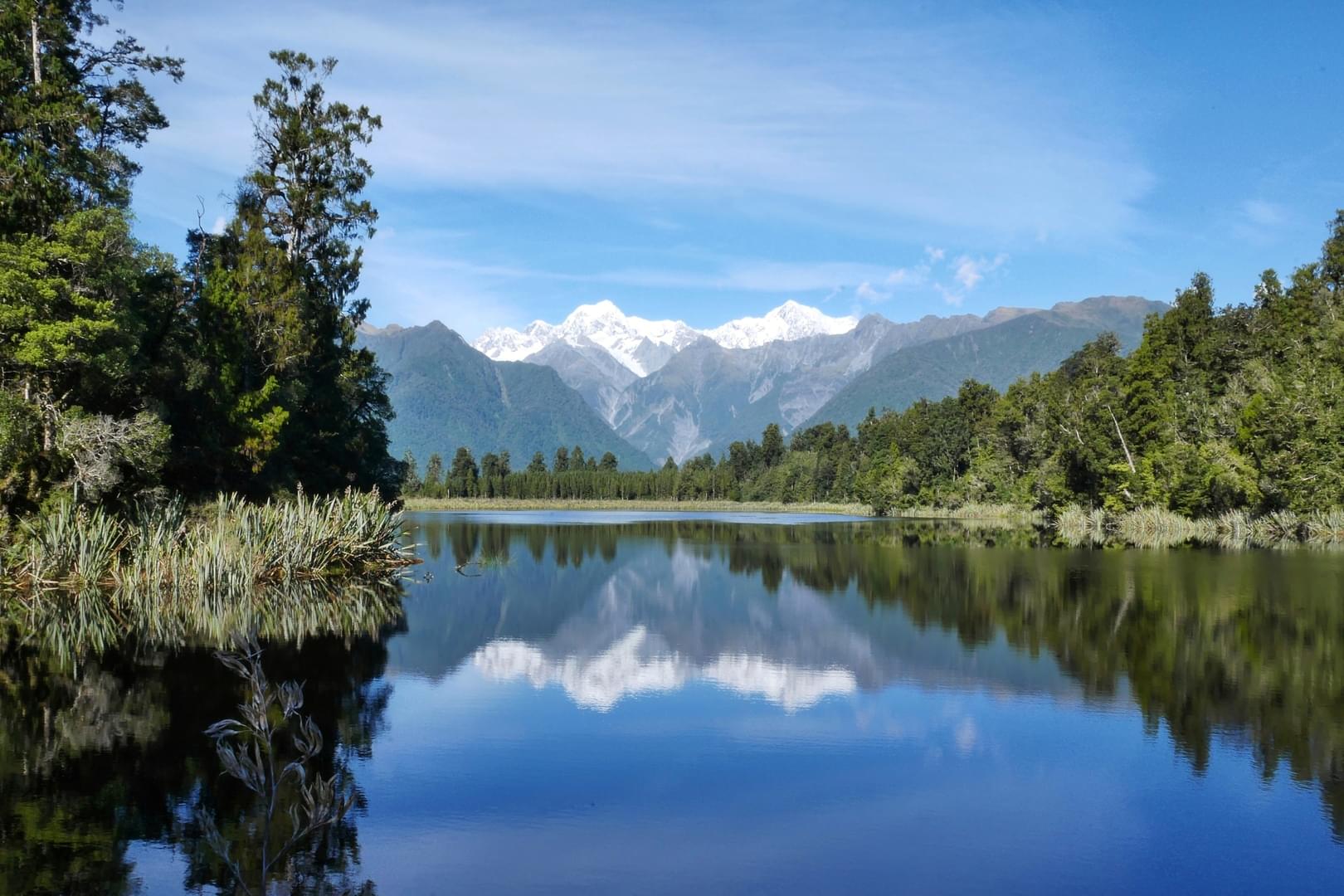 Lake reflecting snow-capped mountains and forest on a sunny day.