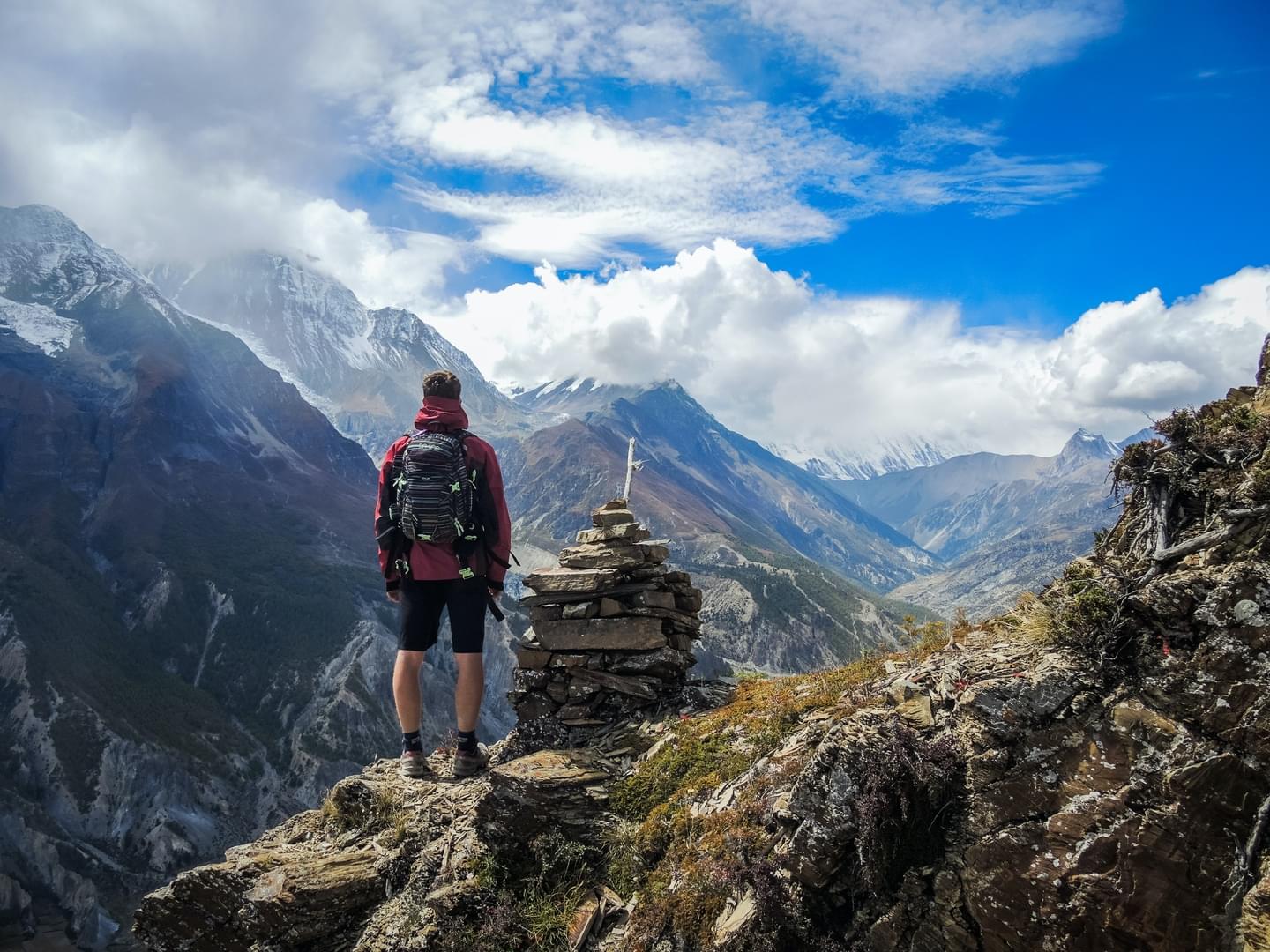Backpacker on a mountain ridge by a stone cairn overlooking mountains.